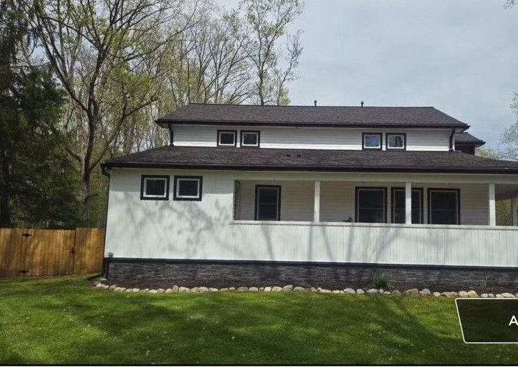 A white house with a black roof and a porch is for sale.