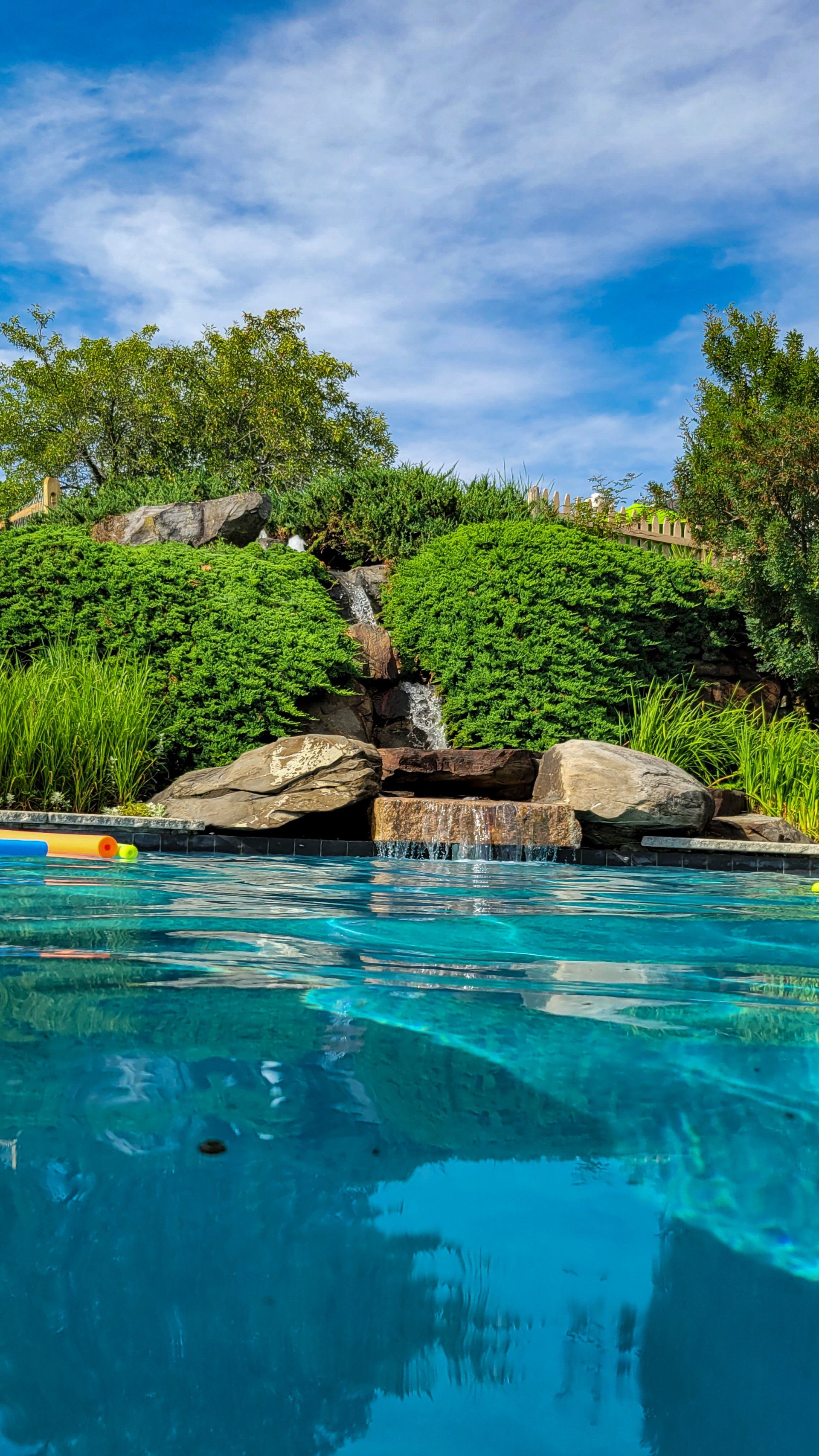 A swimming pool with a waterfall and trees in the background.
