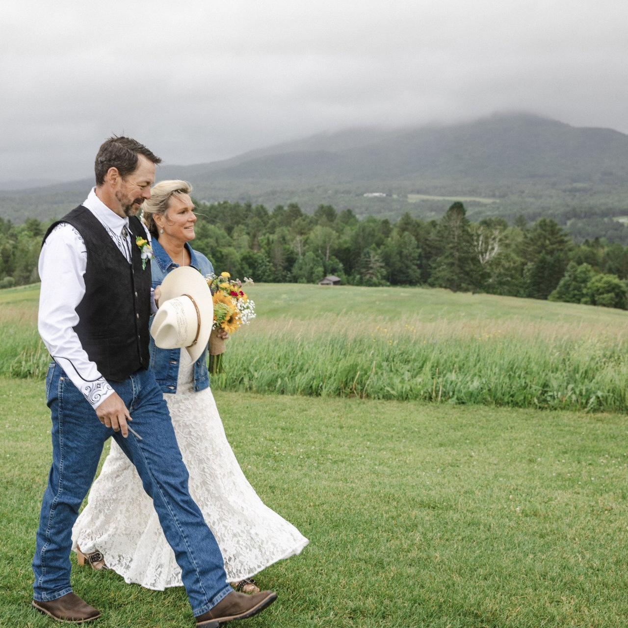 A bride and groom are walking through a grassy field