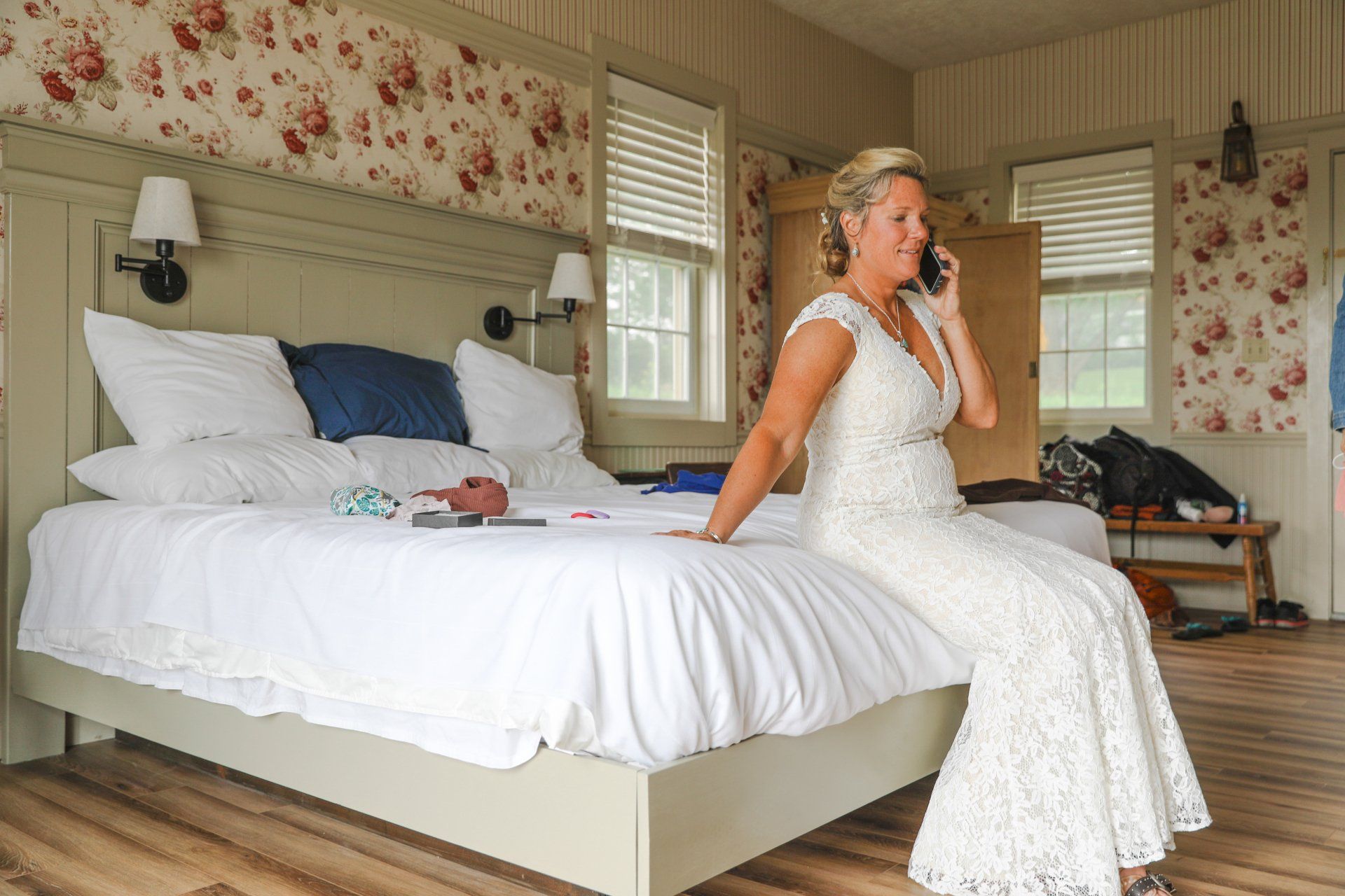 A bride sits on the bed in The Schoolhouse while on the phone with her groom at The Wildflower