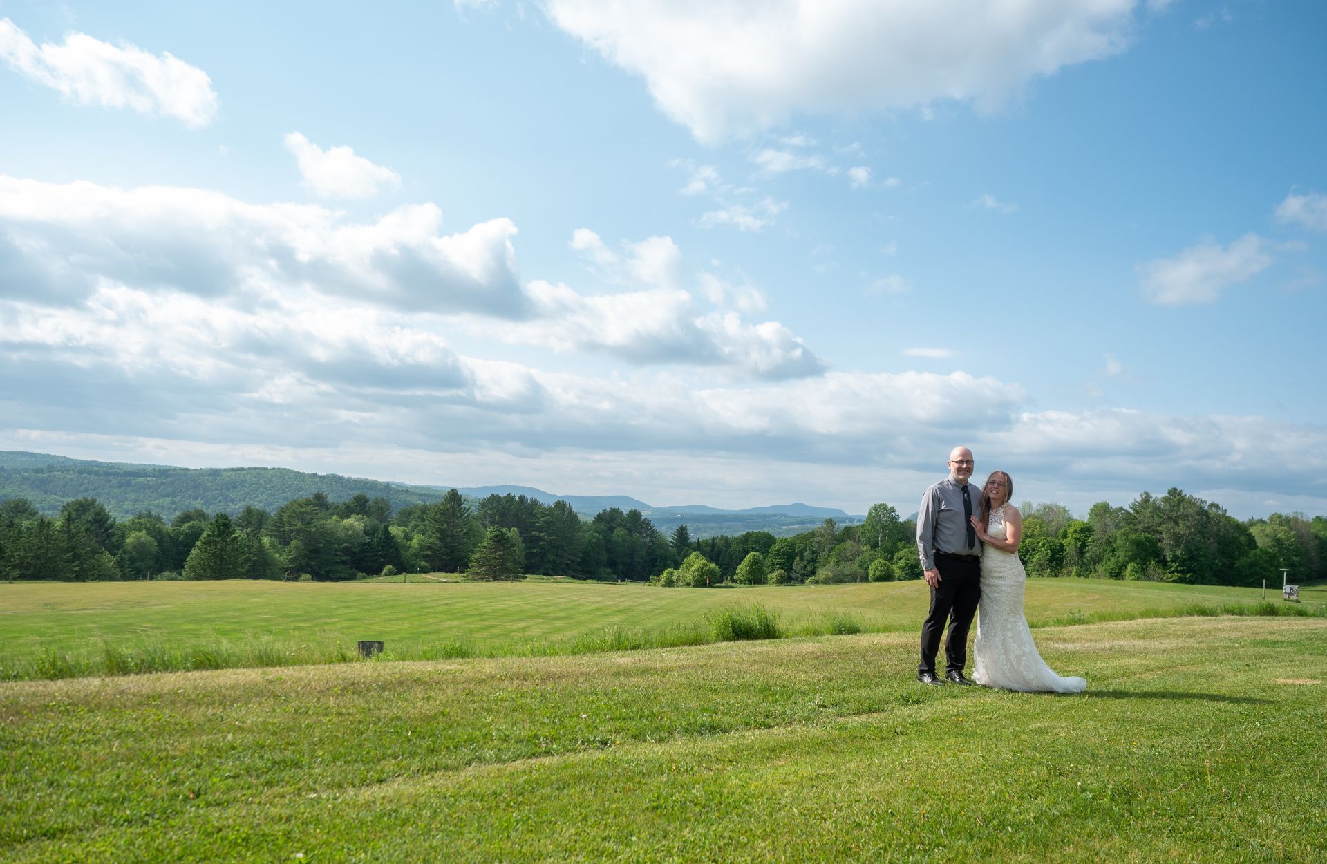 A bride and groom are standing in a grassy field.