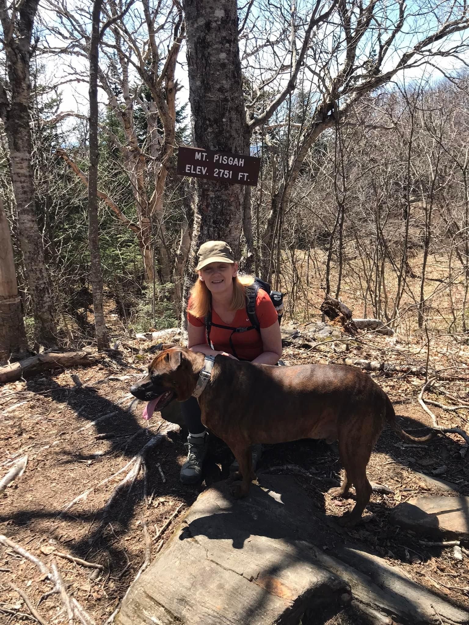 Jenifer with a dog in front of a Mount Pisgah trail sign.