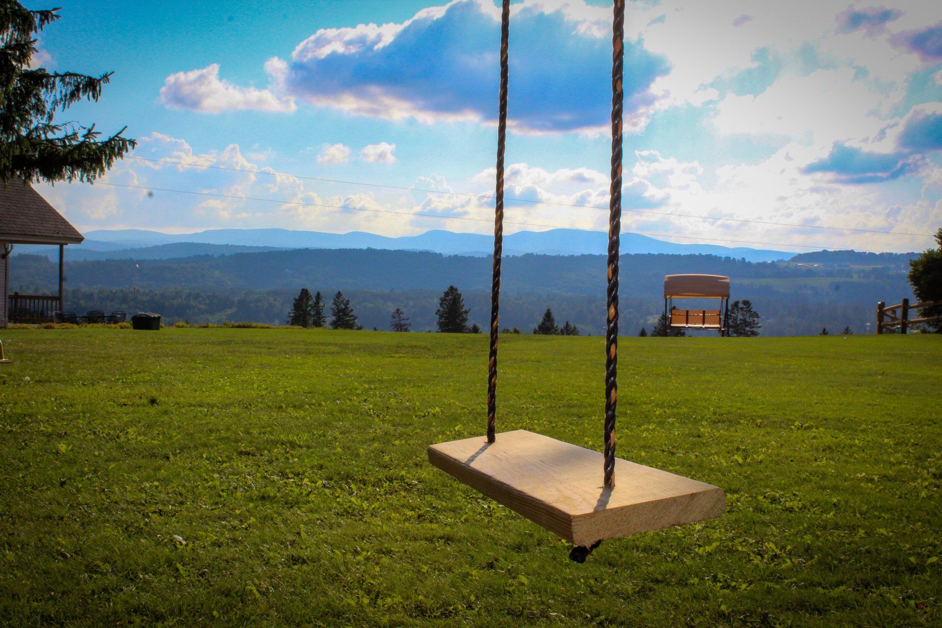 A wooden swing is sitting in the middle of a grassy field.