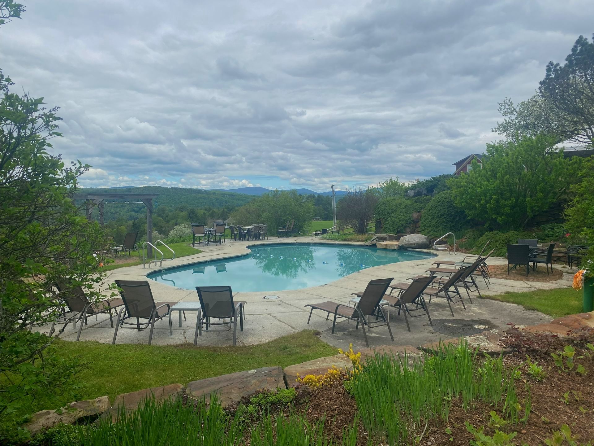 A large swimming pool is surrounded by lawn chairs on a cloudy day
