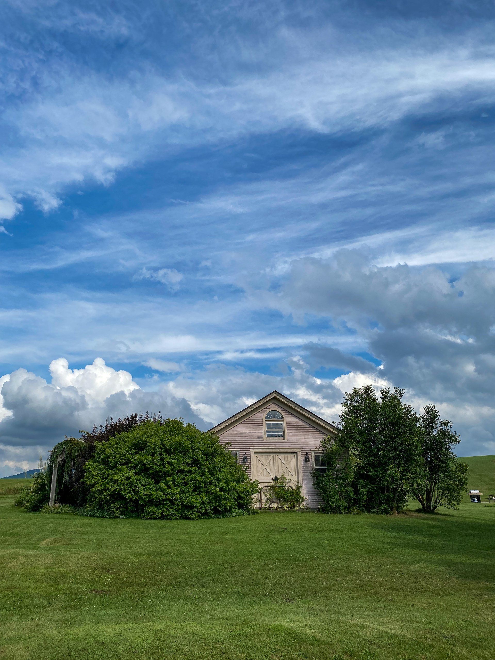 A building on The Wildflower's grounds surrounded by trees, green hills, and a beautiful cloudy sky