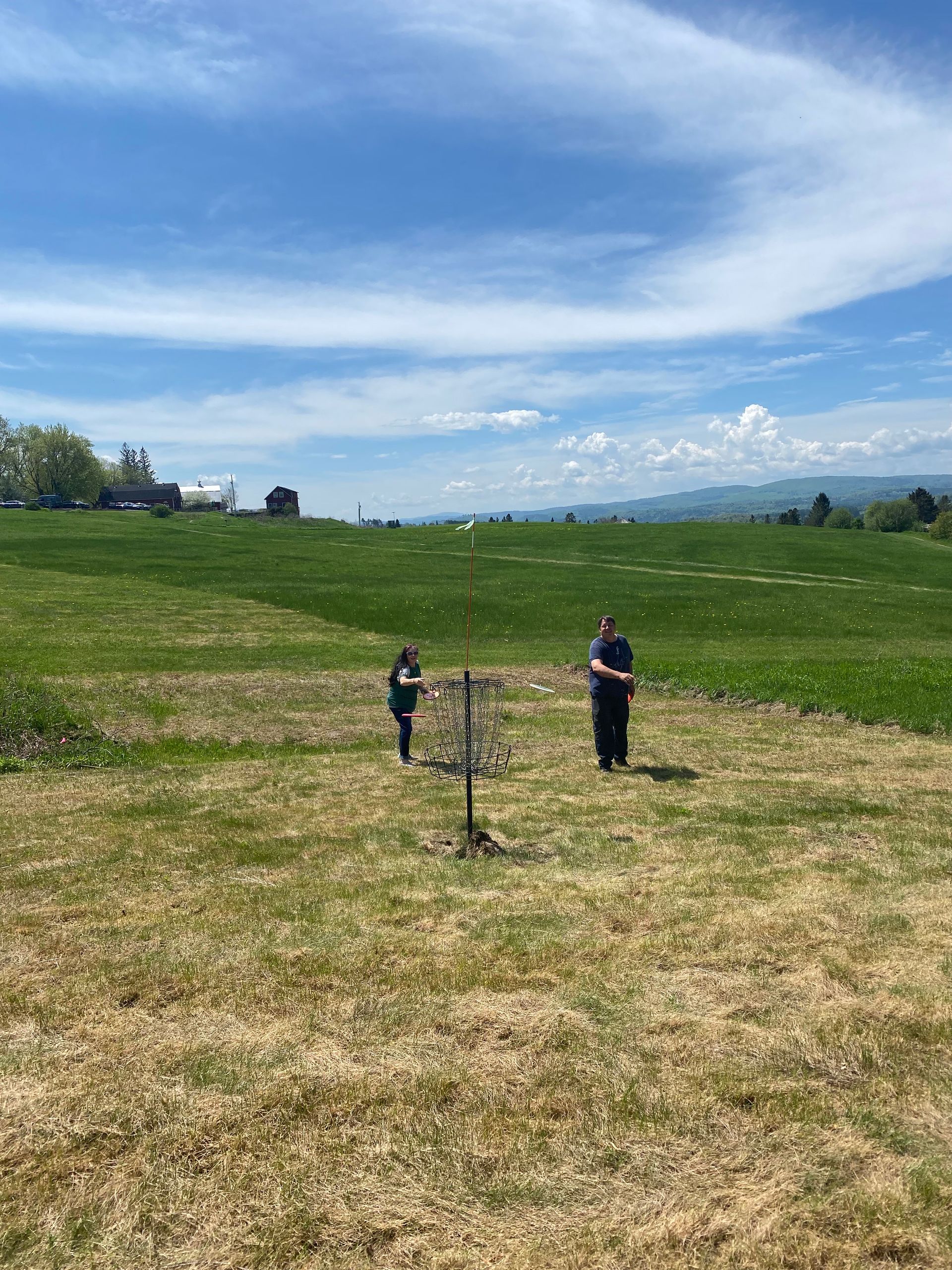 Two people are playing frisbee golf in a grassy field at the Wildflower Inn.