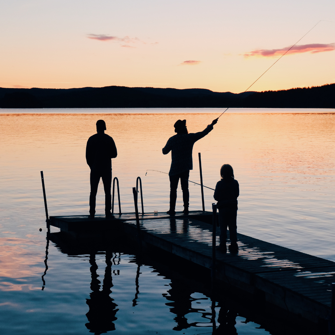 Three people fishing on a dock at sunset