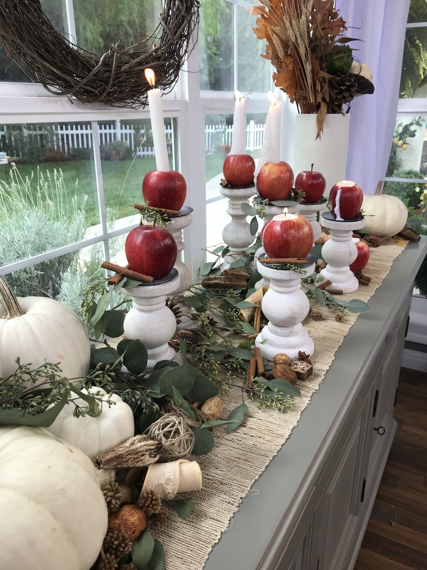 Table covered in pumpkins, eucalyptus, and apples carved into candle holders
