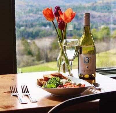 A bottle of wine is sitting on a table next to a bowl of food and a vase of flowers.