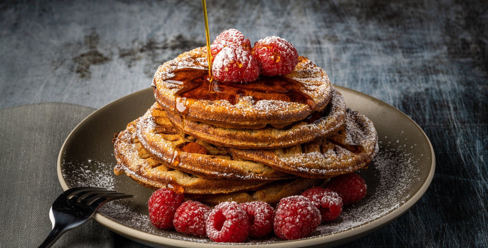 Delicious pancakes covered in raspberries and powdered sugar with syrup