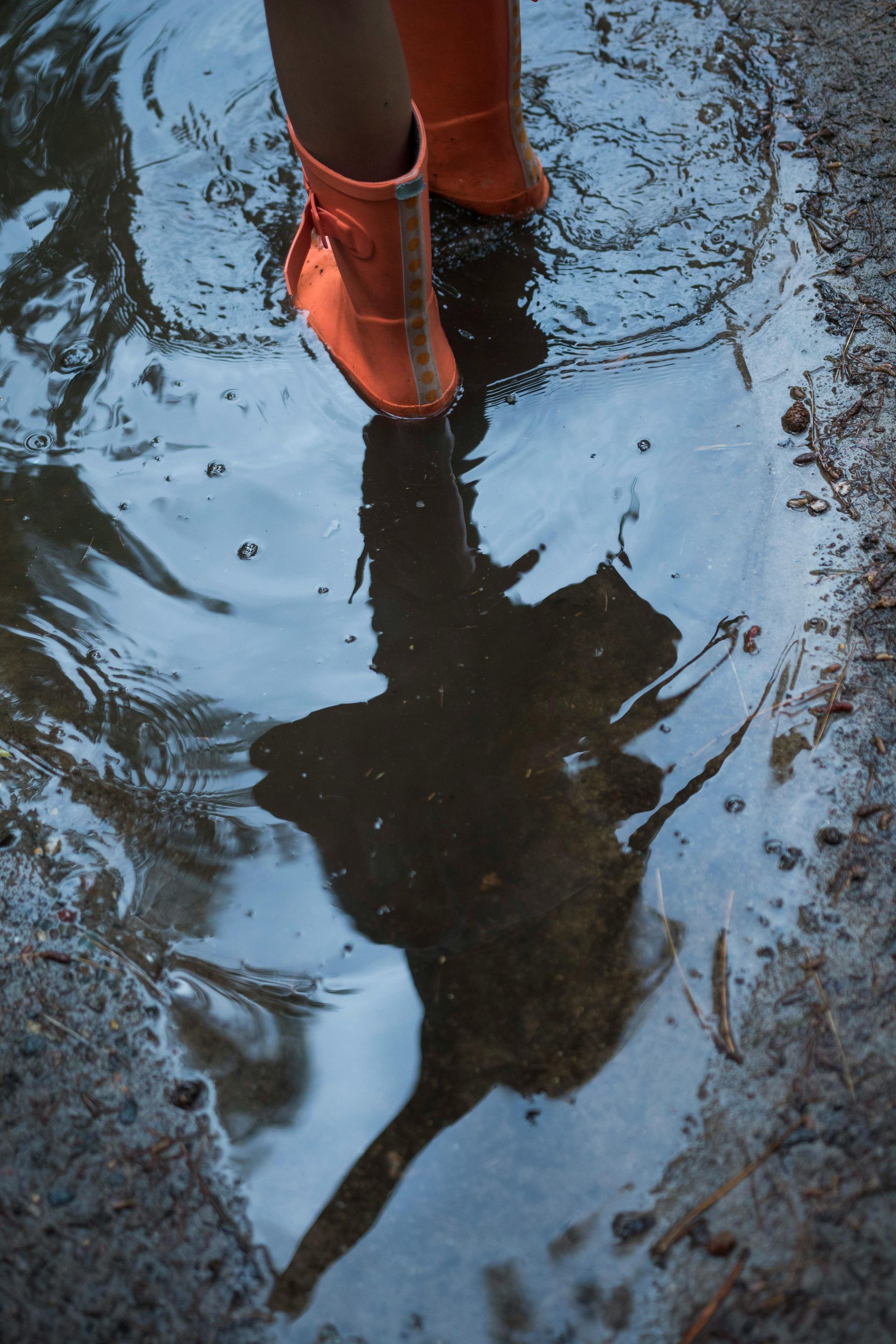 Orange boots in a puddle, reflecting a blurry figure and the sky.