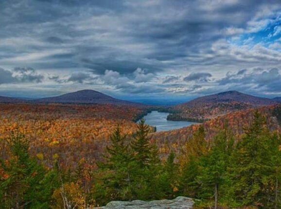 A lake surrounded by mountains and trees with a cloudy sky in the background.