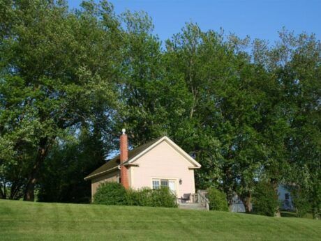 A small house sits on top of a grassy hill surrounded by trees