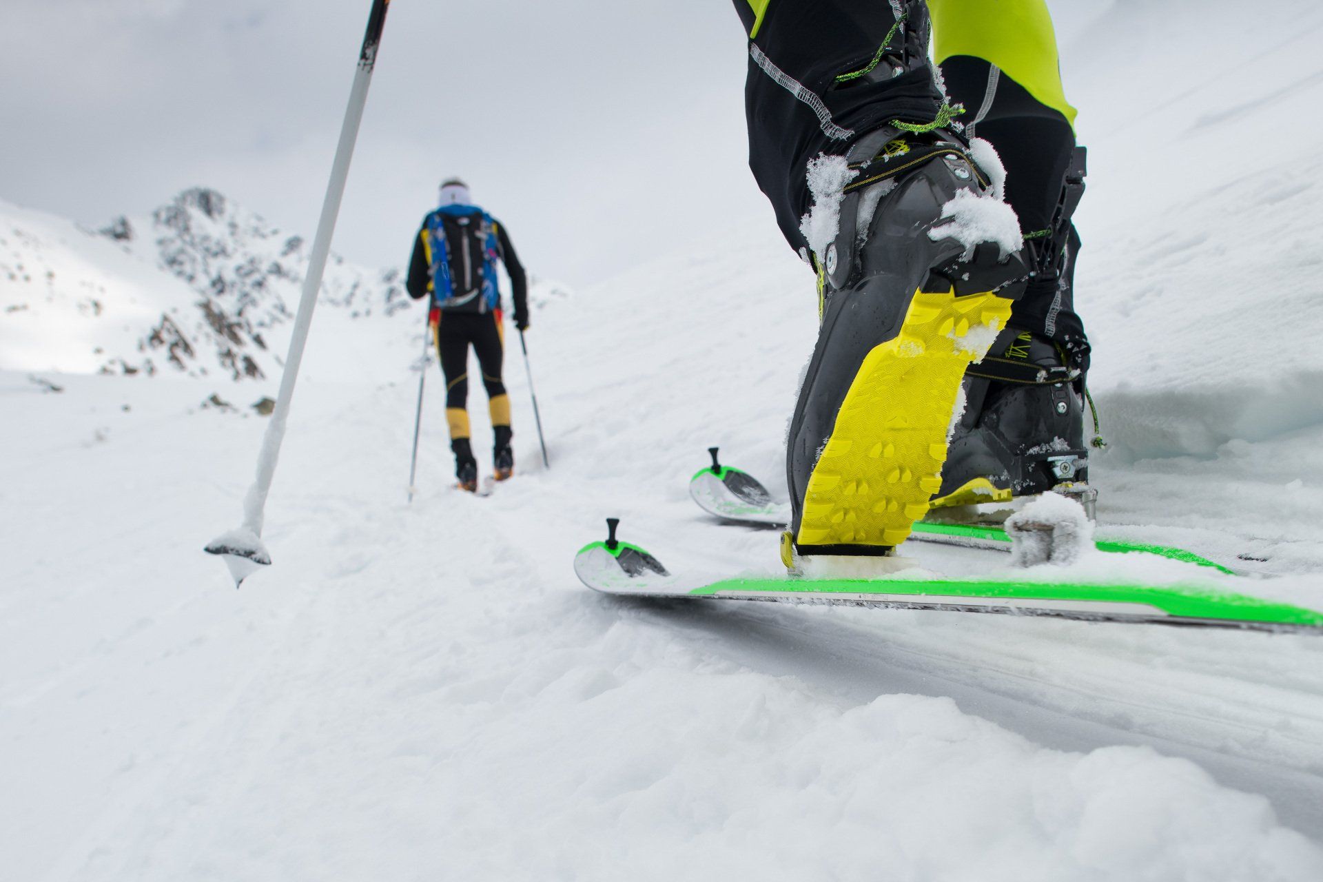Two people ski mountaineering with a close-up of a ski boot