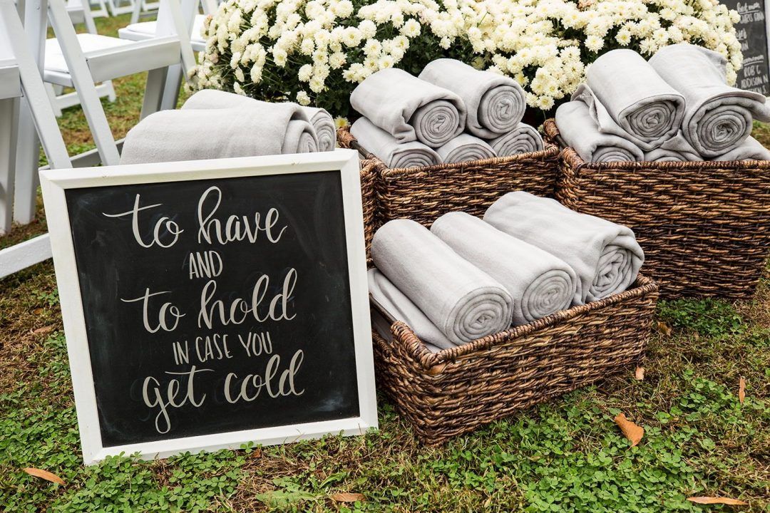 Baskets full of Blankets for wedding guests next to a sign that reads 