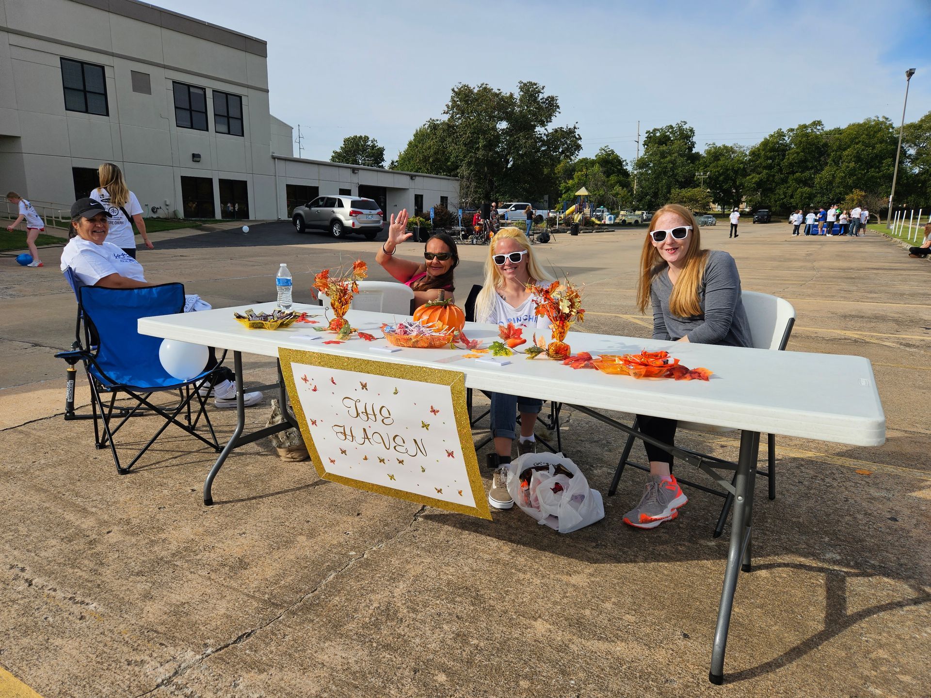 A group of people are sitting at a table in a parking lot.