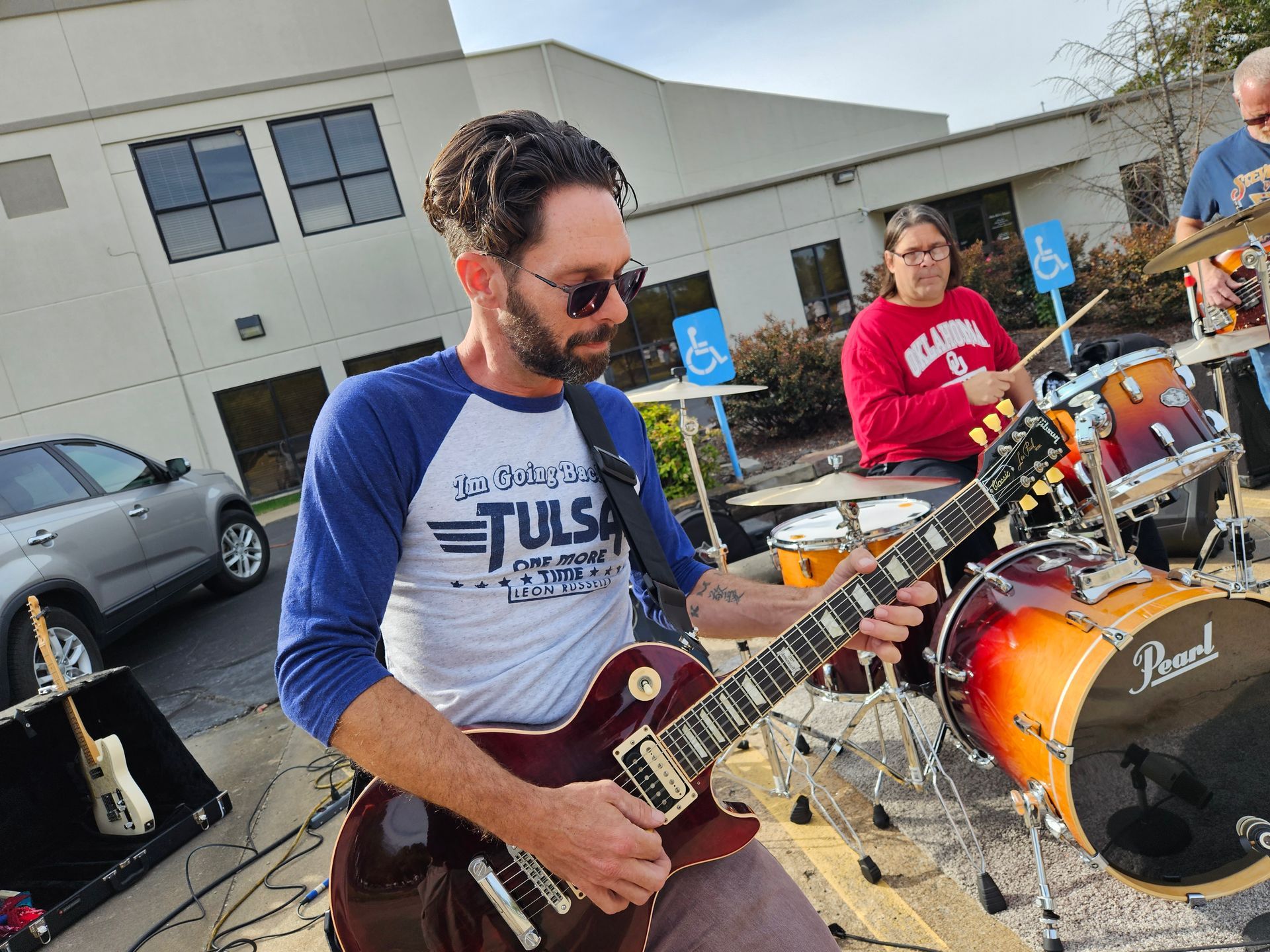 A man in a tulsa shirt is playing a guitar in front of a drum set.