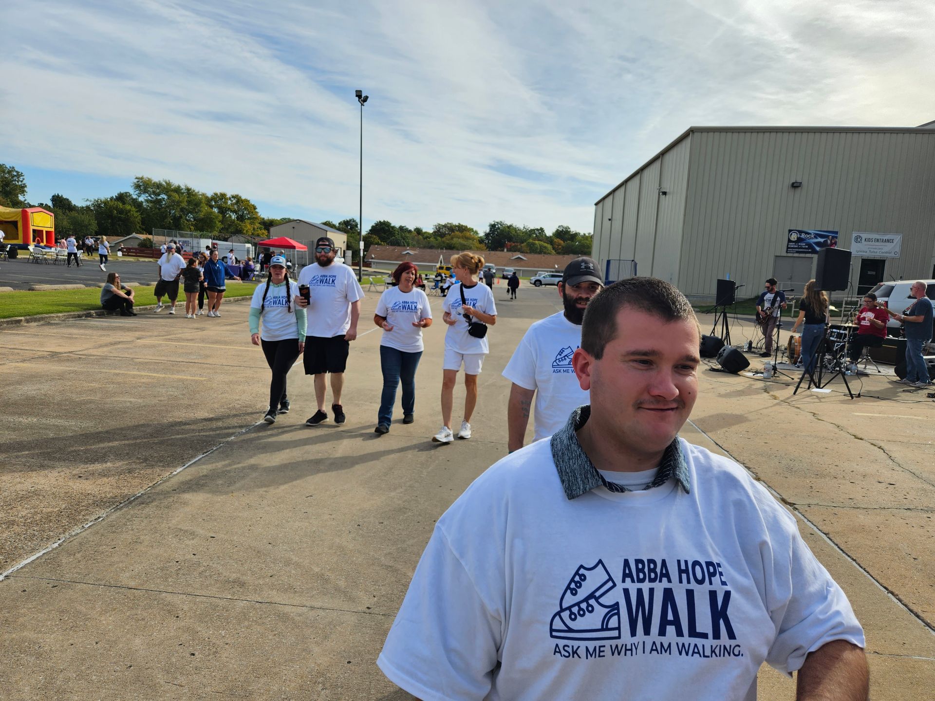 A man wearing an abba hoff walk shirt stands in front of a group of people