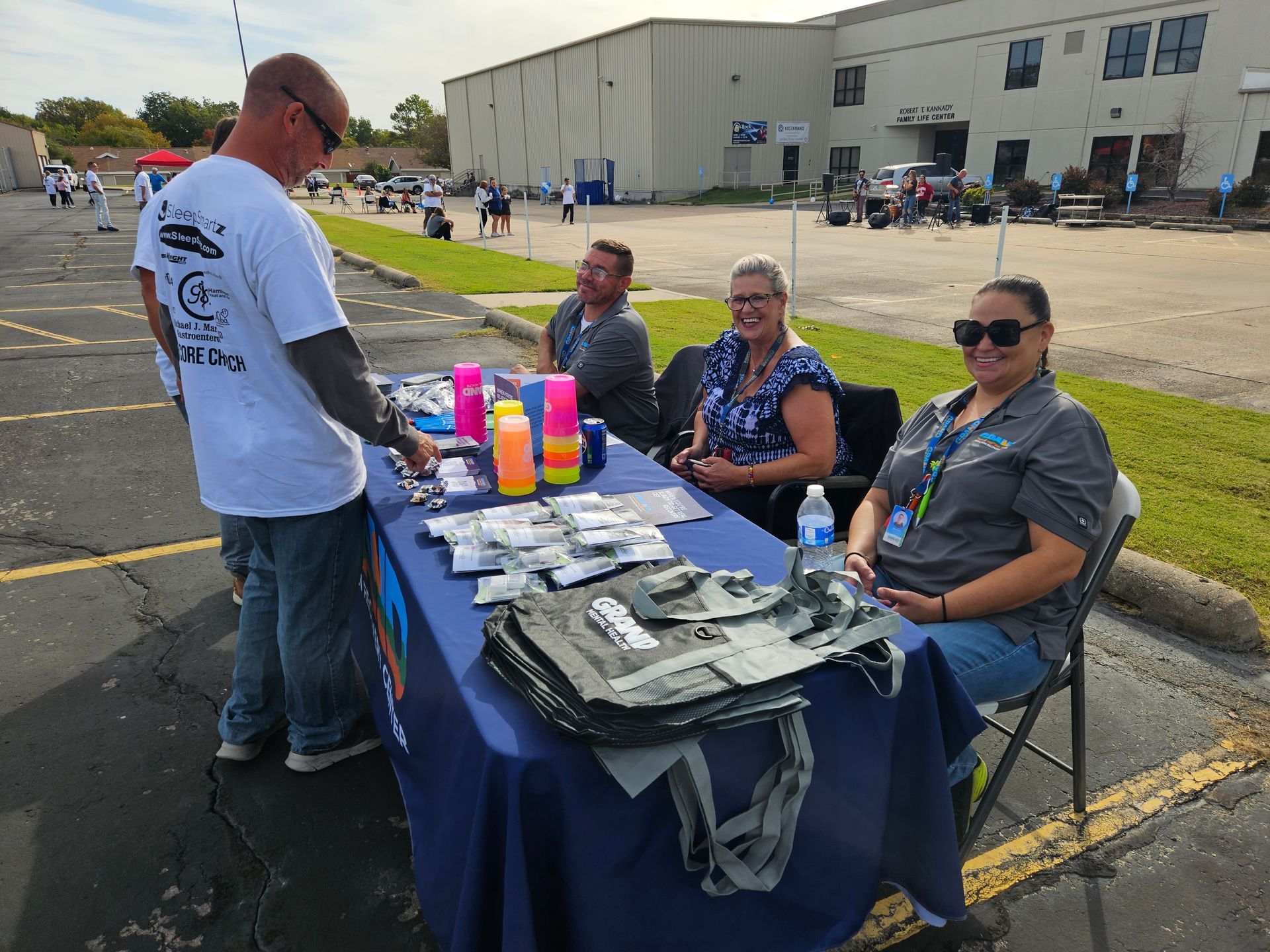 A group of people are sitting at a table in a parking lot.