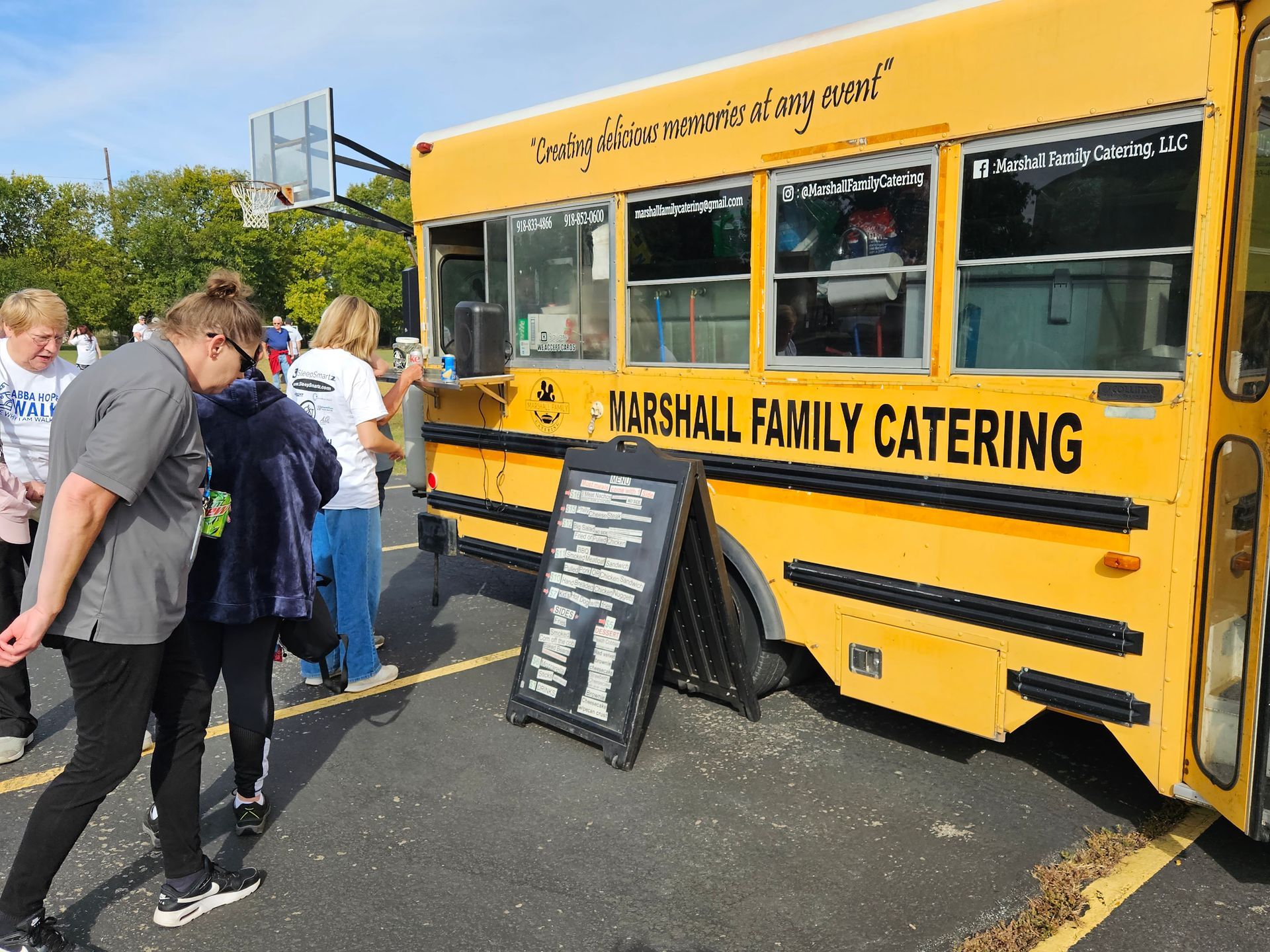 A group of people are standing in front of a yellow bus that says marshall family catering