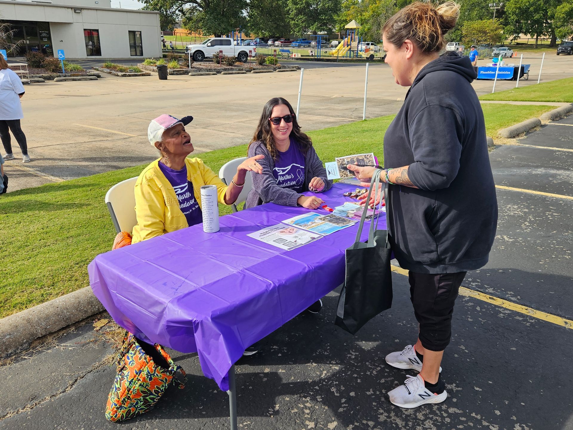 Two women are sitting at a table in a parking lot talking to each other.