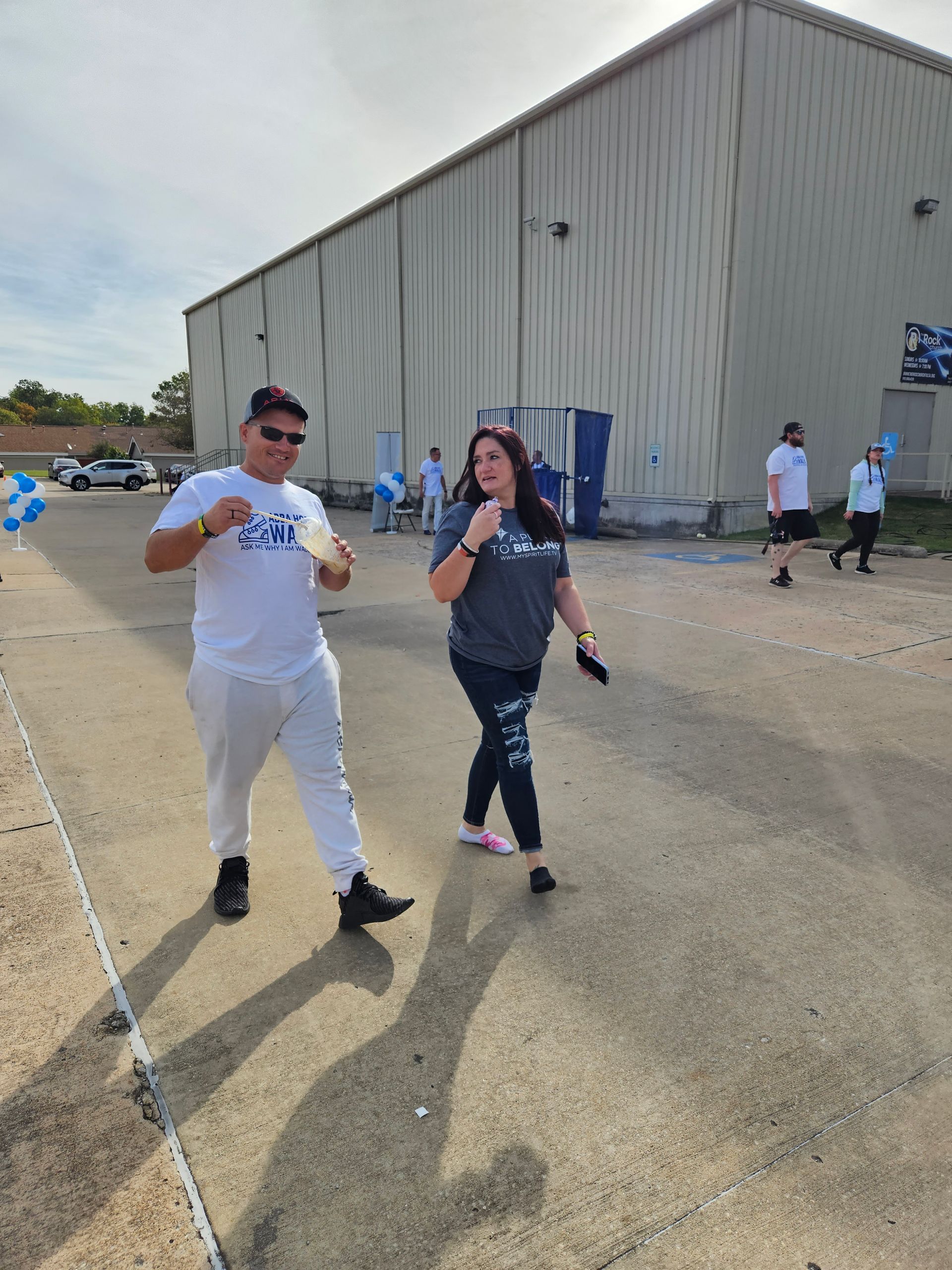 A man and a woman are walking down a street in front of a building.
