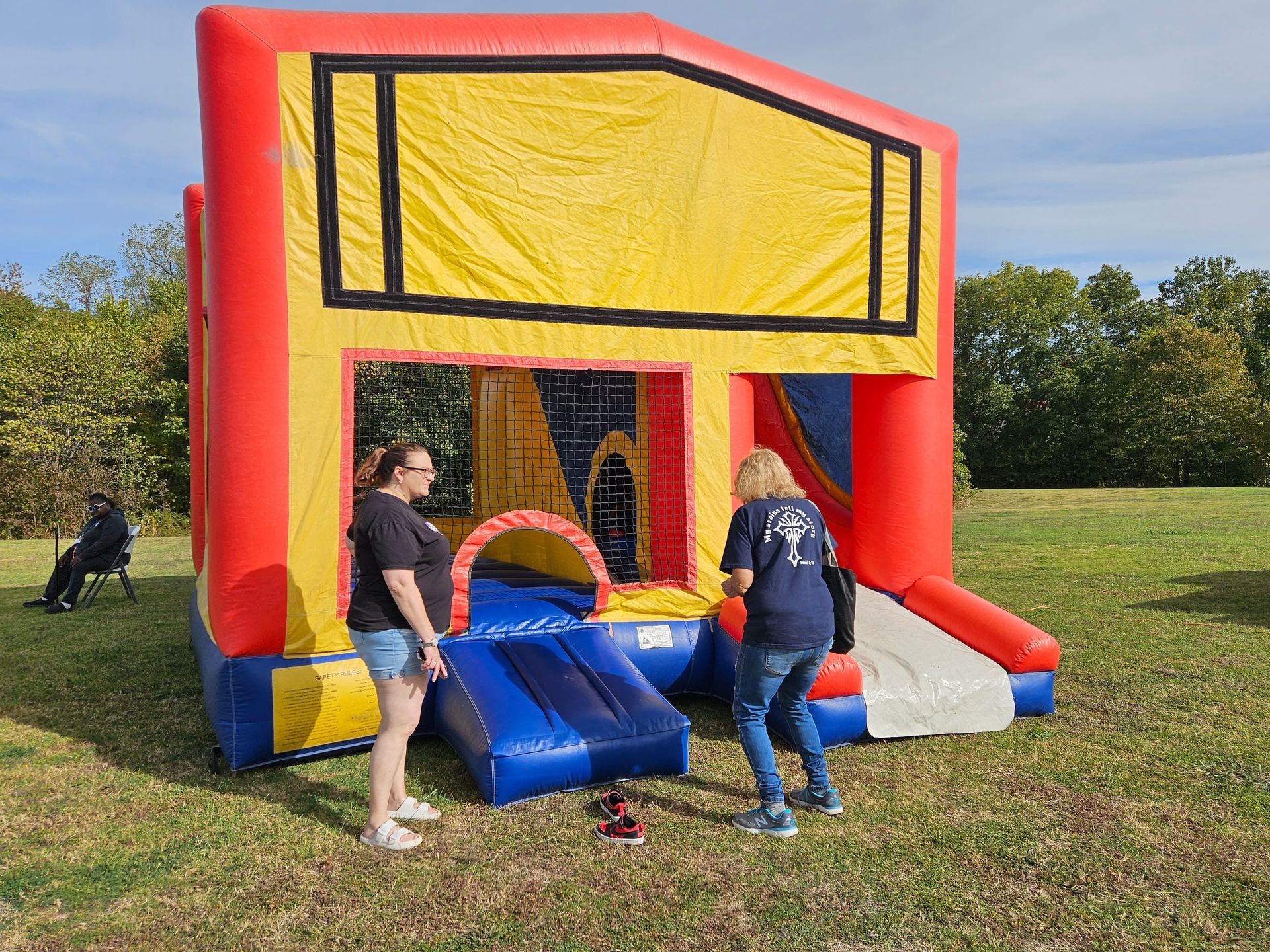 Two women are standing next to a bouncy house in a field.