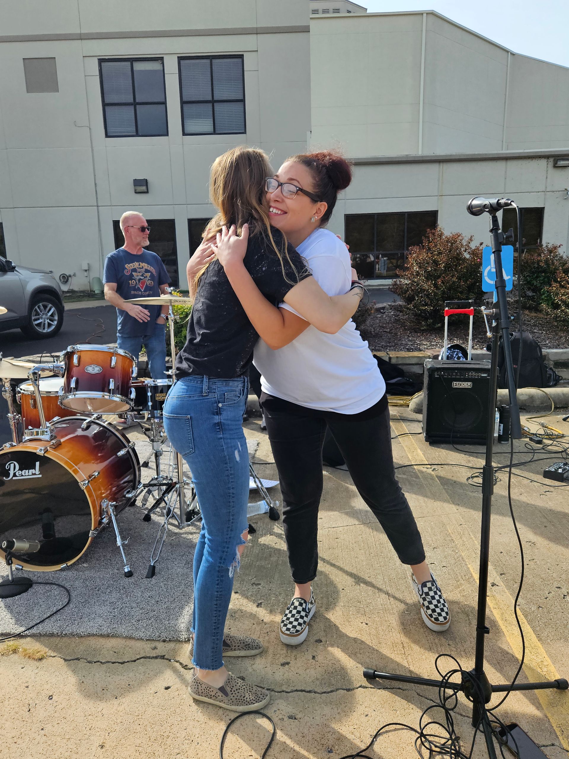 Two women hugging each other in front of a drum set