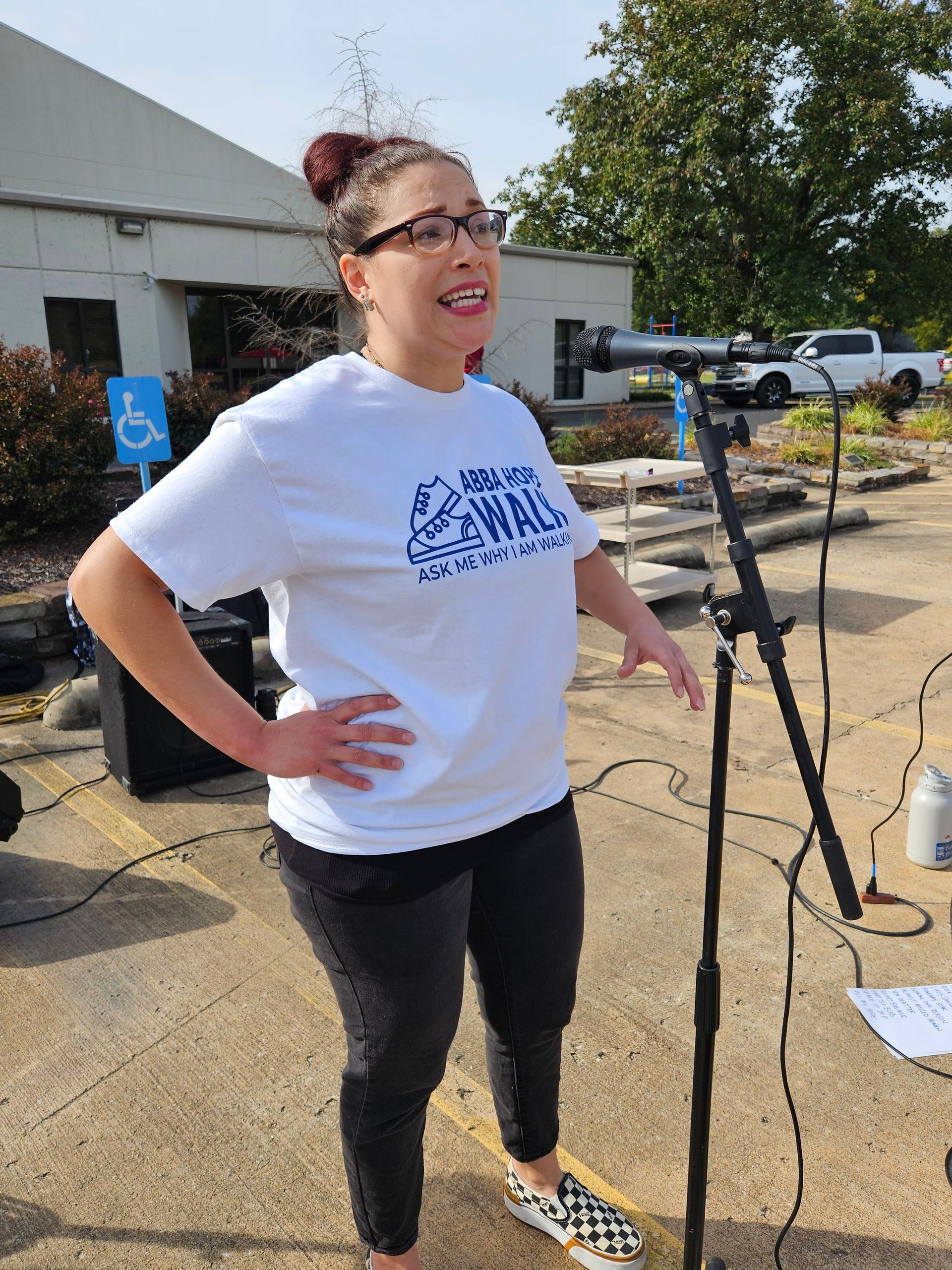 A woman in a white shirt is standing in front of a microphone.