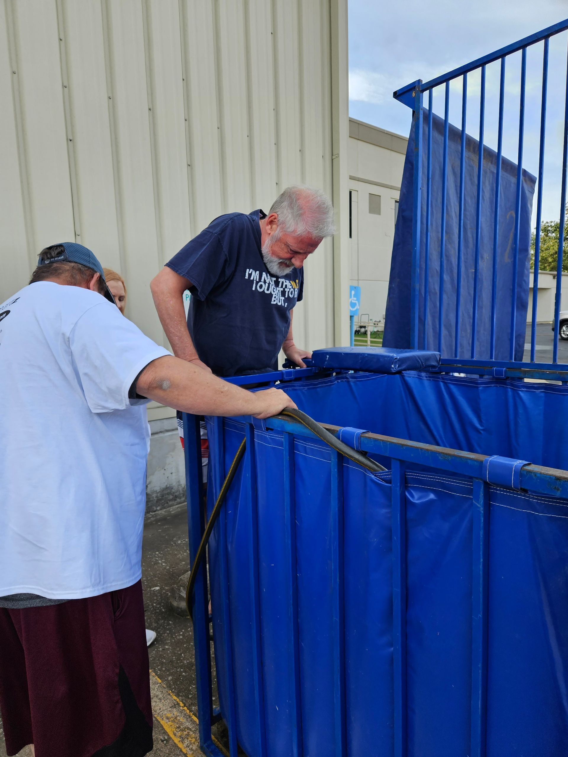 Two men are working on a blue container with a hose attached to it.