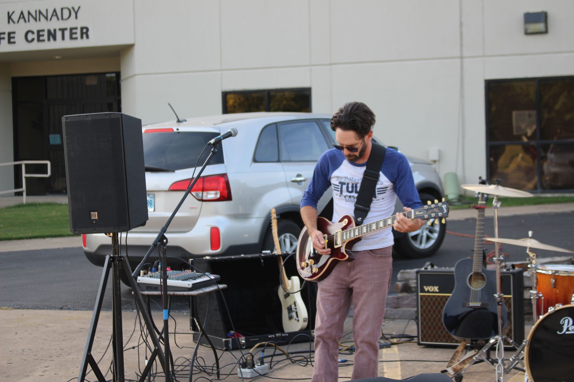 A man is playing a guitar in front of a building that says kannady life center