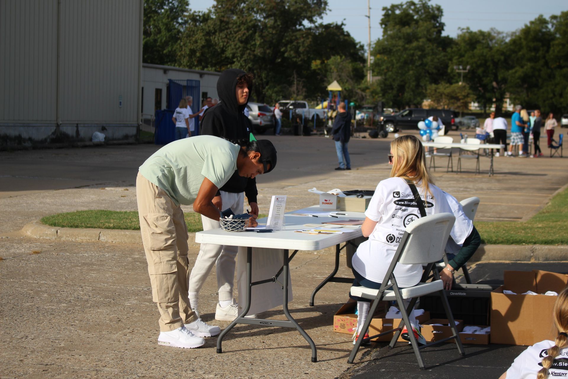 A group of people are standing around a table in a parking lot.