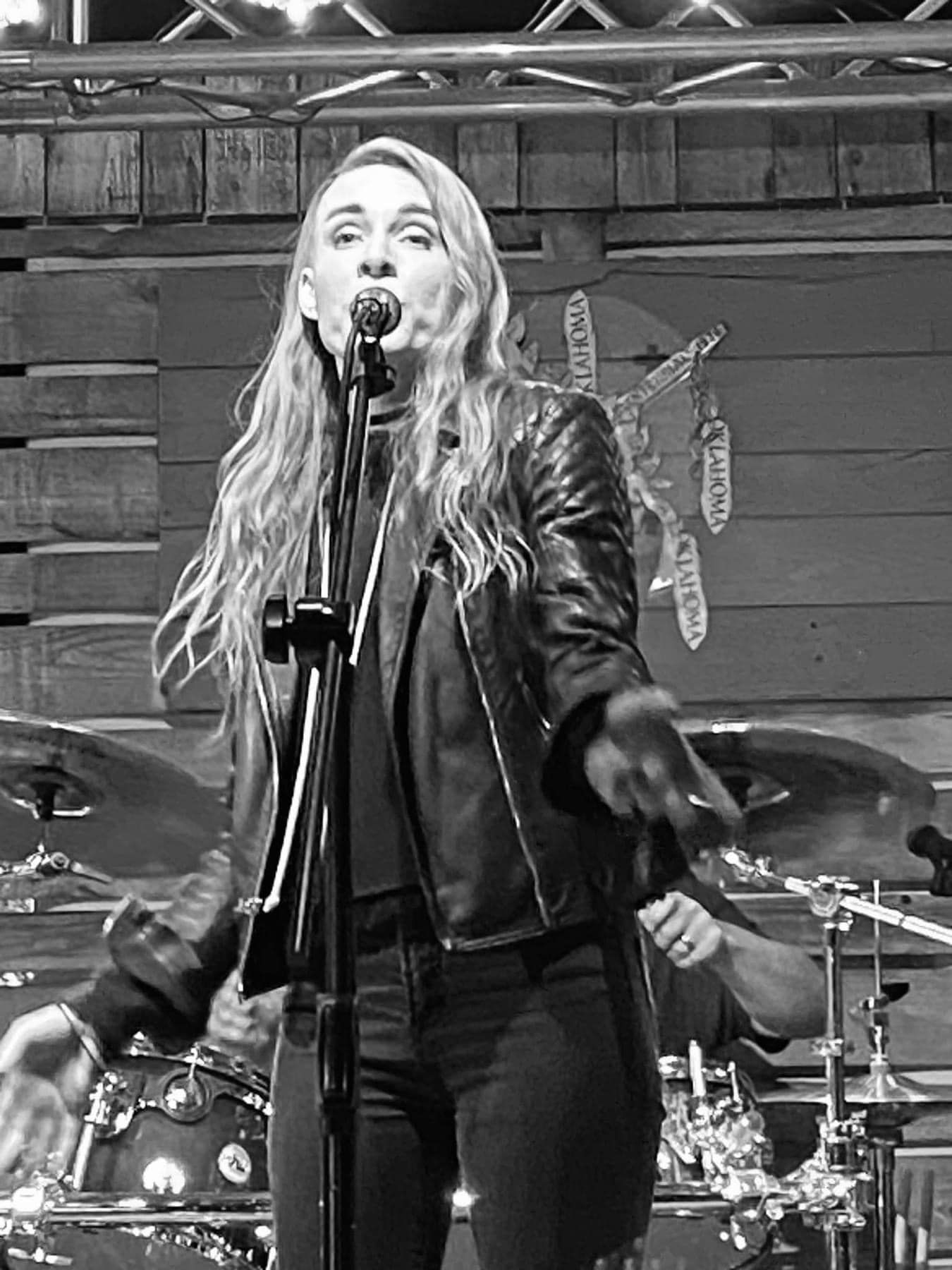 A woman is singing into a microphone on stage in a black and white photo.