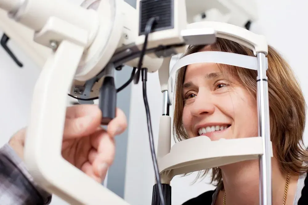 A woman is smiling while having her eyes examined by an ophthalmologist.