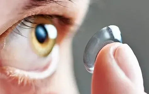 A close up of a person holding a contact lens in front of their eye.
