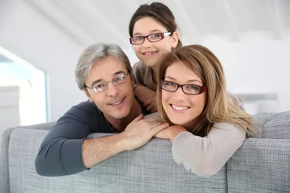 A family wearing glasses is sitting on a couch.