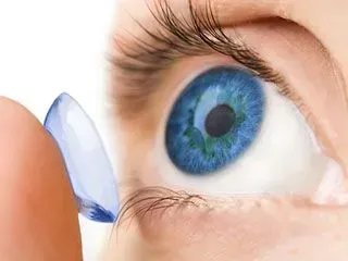 A close up of a person putting a contact lens in their blue eye.