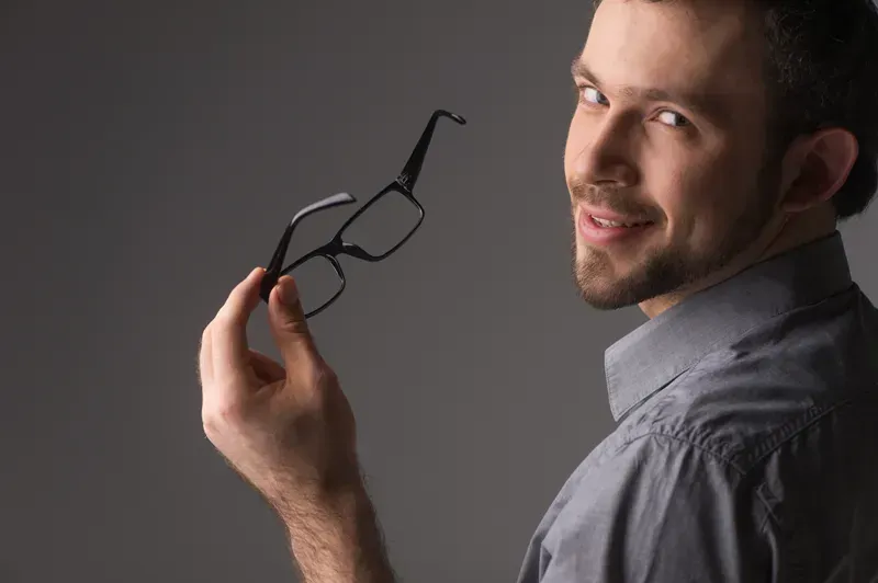 A man is holding a pair of glasses in his hand and smiling.