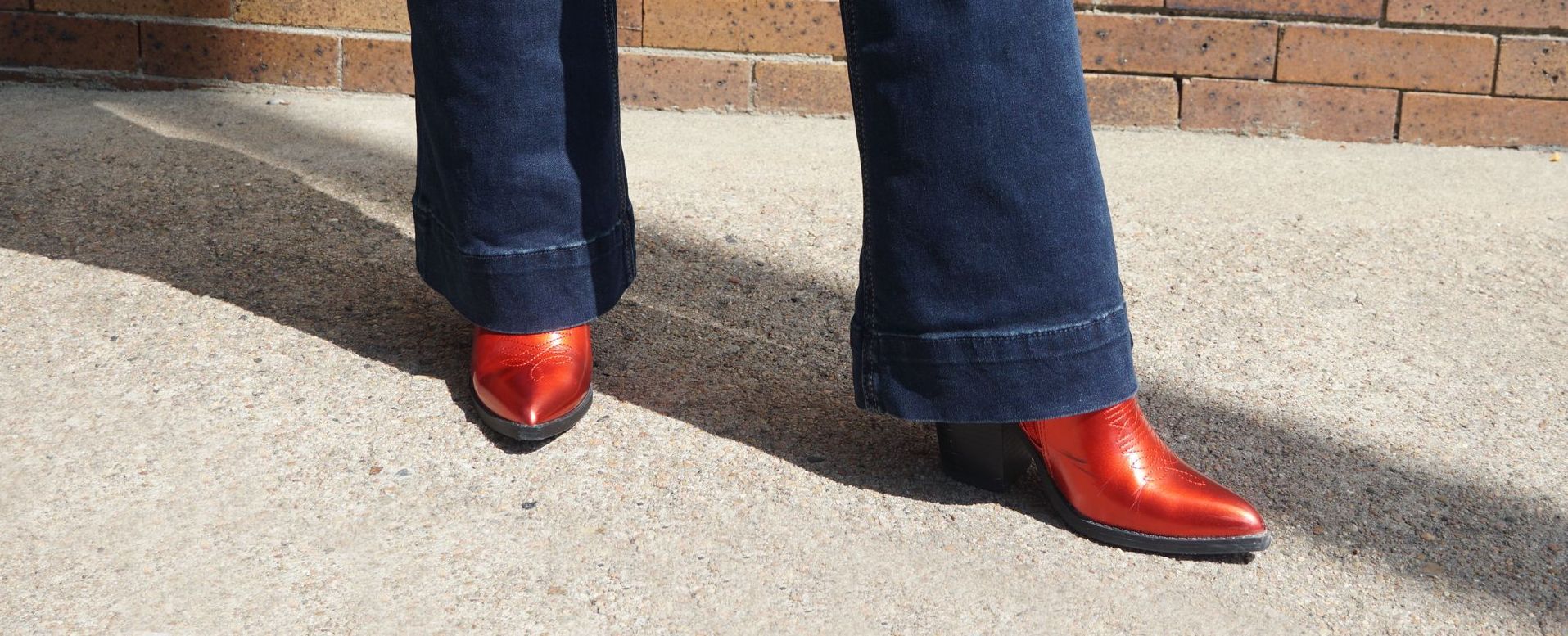 A person wearing red boots and blue jeans is standing on a sidewalk.