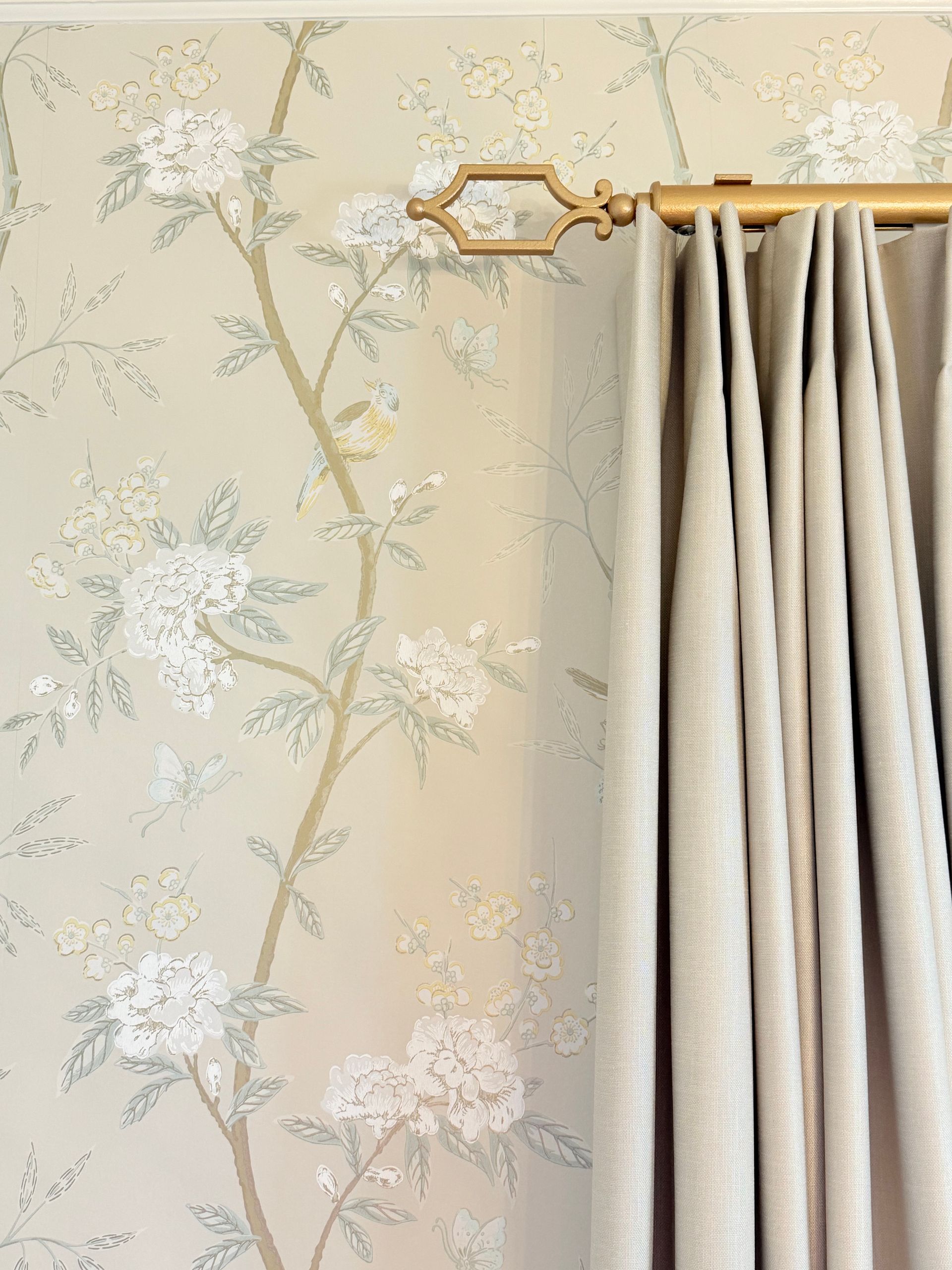 Floral wallpaper beside beige curtains, with a decorative gold curtain rod bracket.