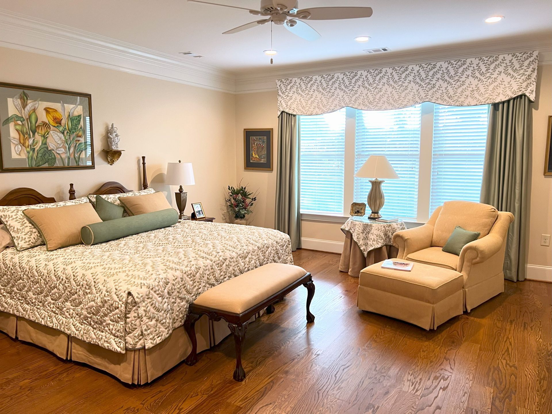 Spacious bedroom with bed, chaise lounge, armchair, and window seat in warm beige tones