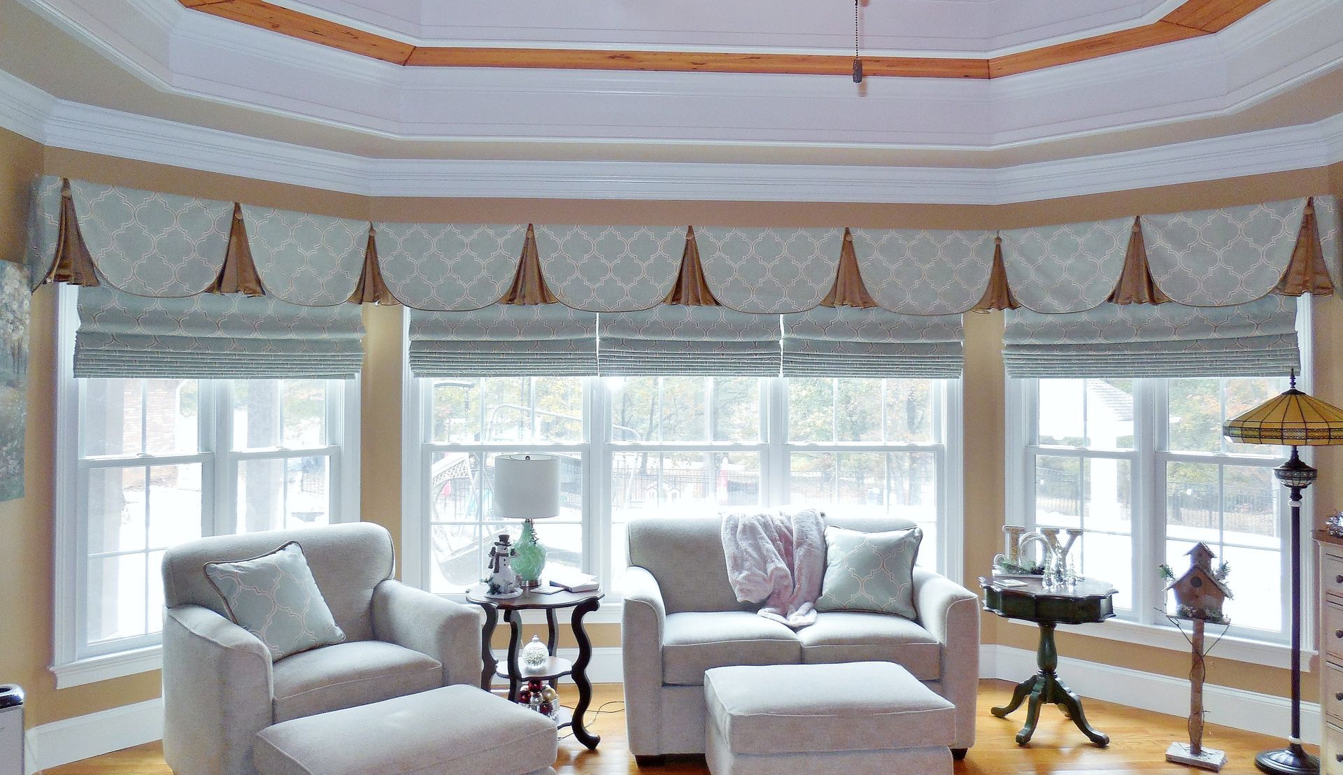 Bright sunroom with white armchairs, side tables, and tall windows with patterned valances