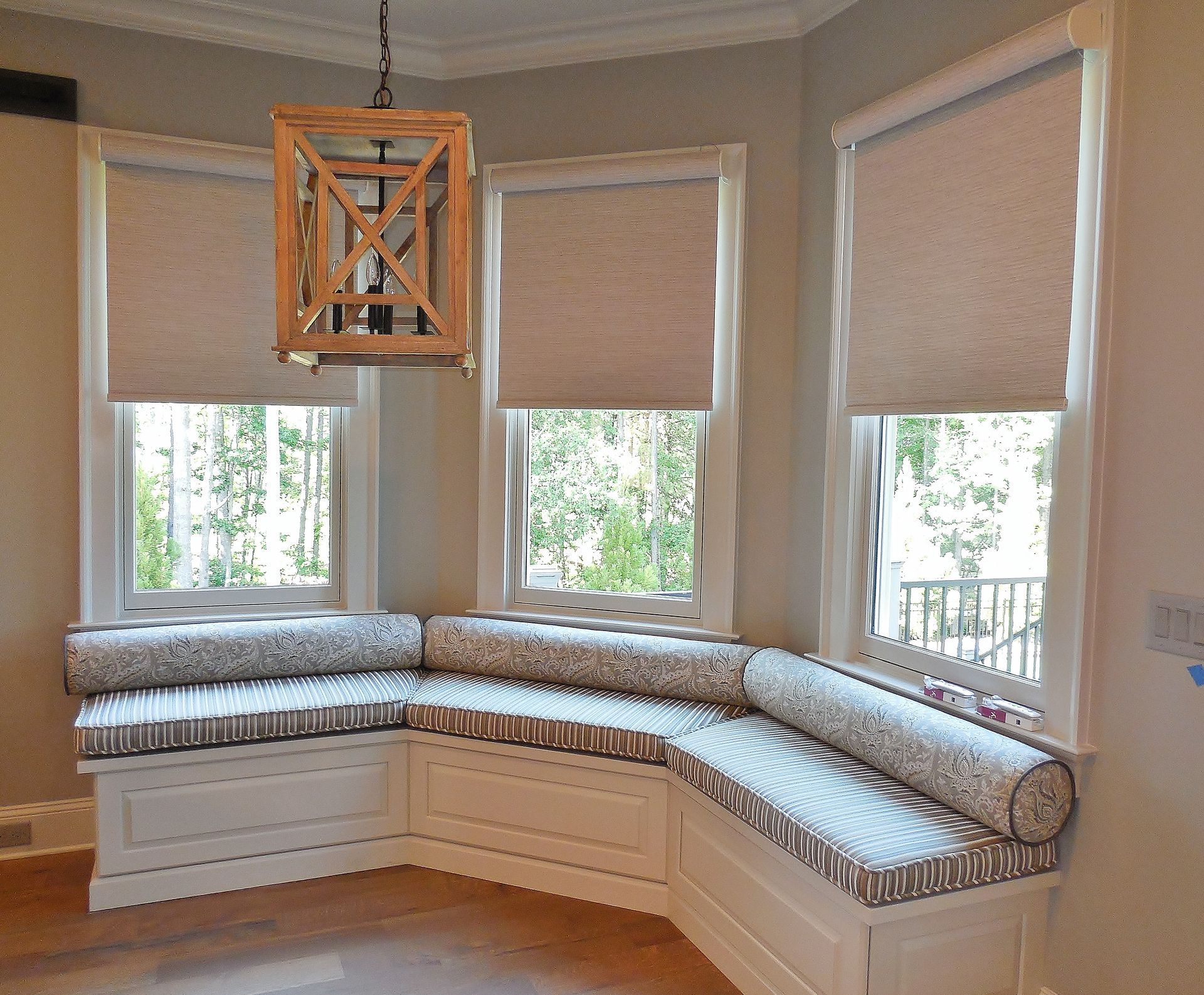 Built-in curved window seat with patterned cushions beneath three large windows in a bright room