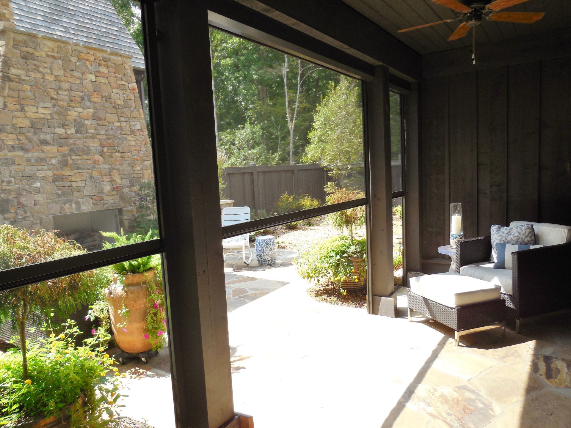 Covered patio with sliding glass doors, stone wall, and outdoor seating overlooking a sunny garden.