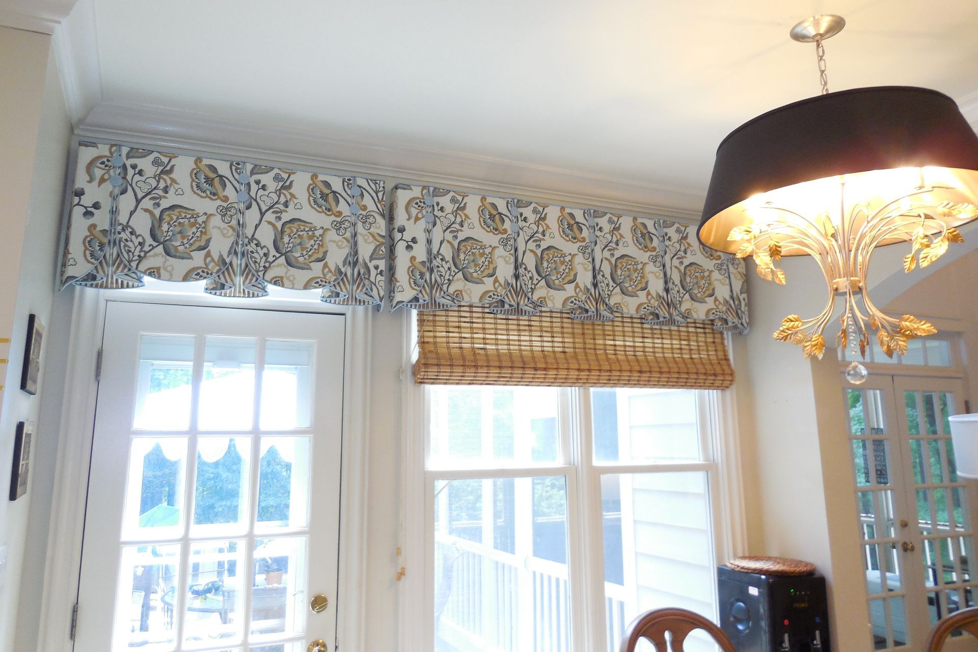 Bright dining room with floral valance, French doors, and a hanging chandelier
