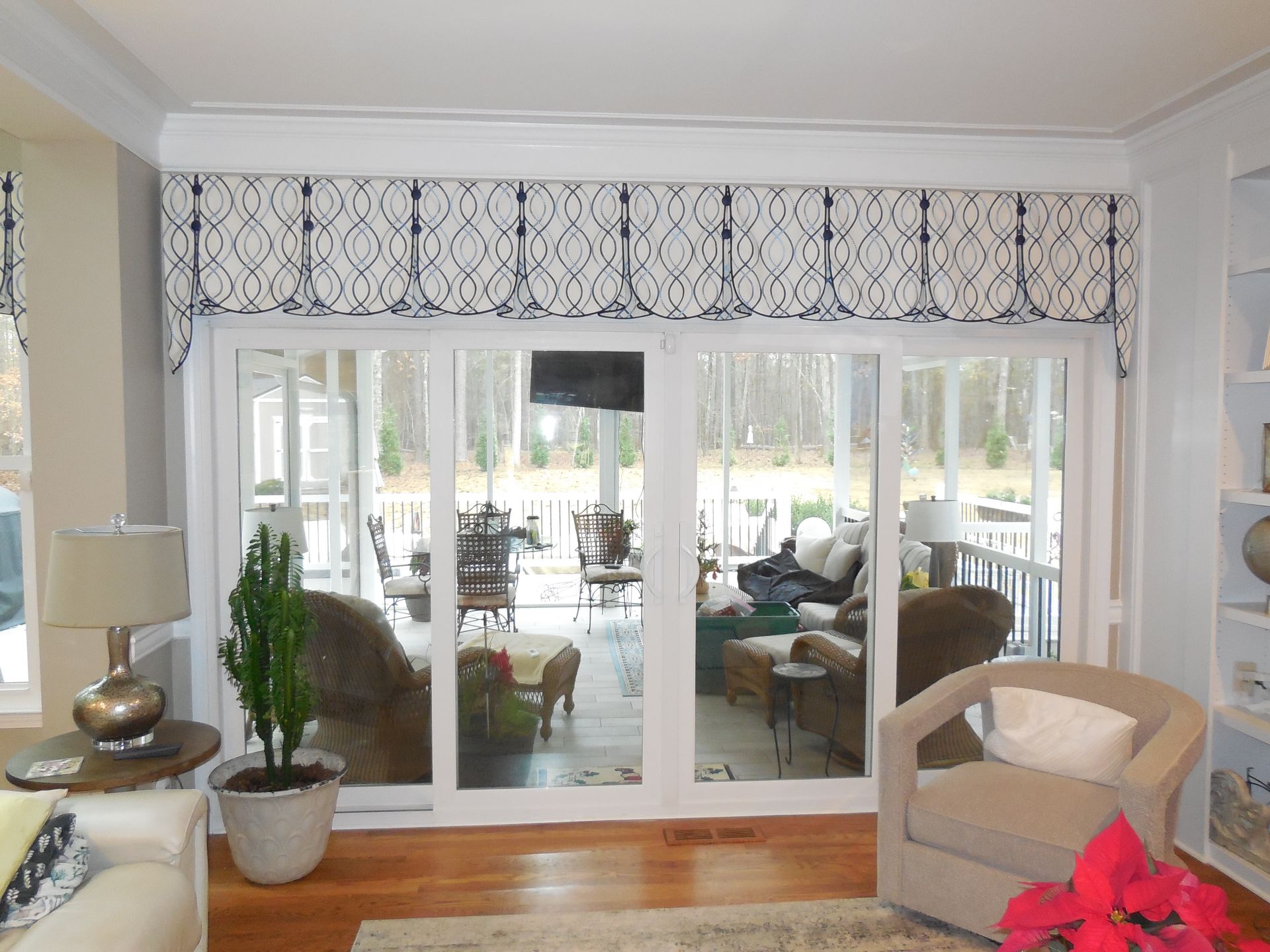 Bright living room with sliding glass doors, patterned valance, and beige armchair facing a sunroom.