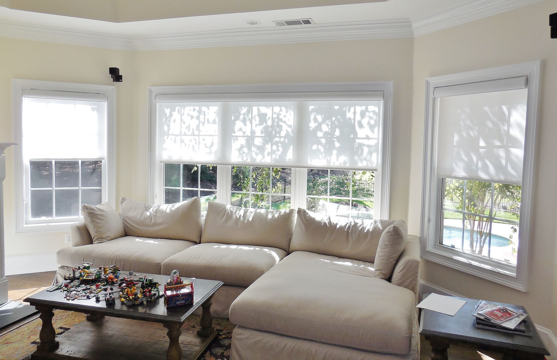 Bright living room with a beige sectional, coffee table, and large windows overlooking a pool.