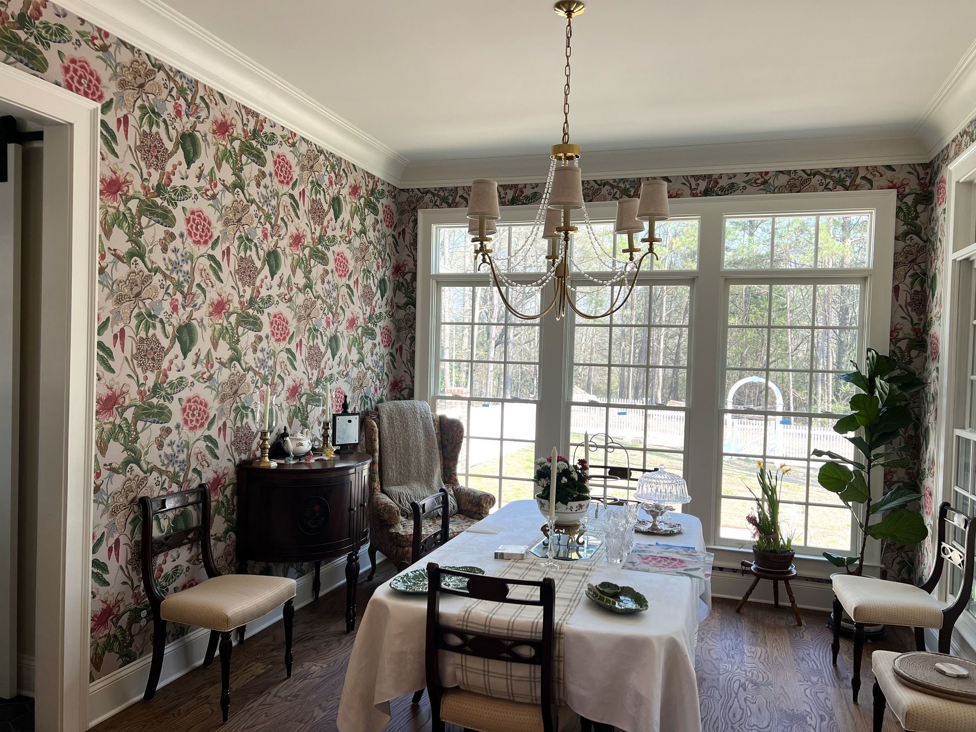 Dining room with floral wallpaper, a long set table, and large windows overlooking a snowy yard