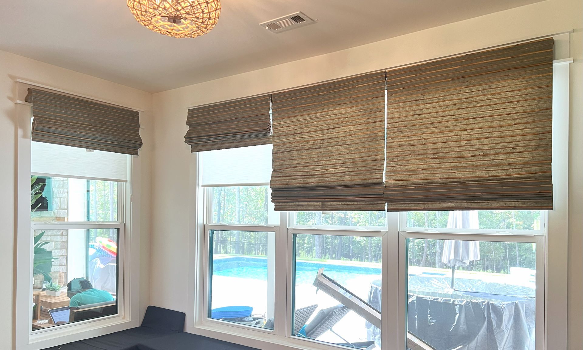 Sunlit room with woven window shades and white-trimmed windows overlooking a deck