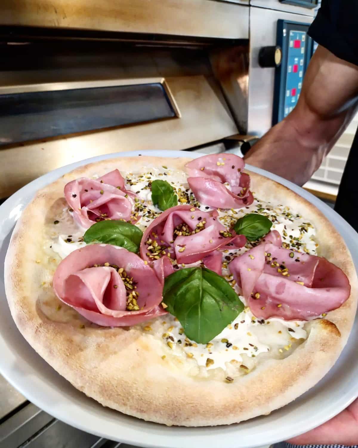 Una persona tiene in mano un piatto bianco con una pizza sopra.